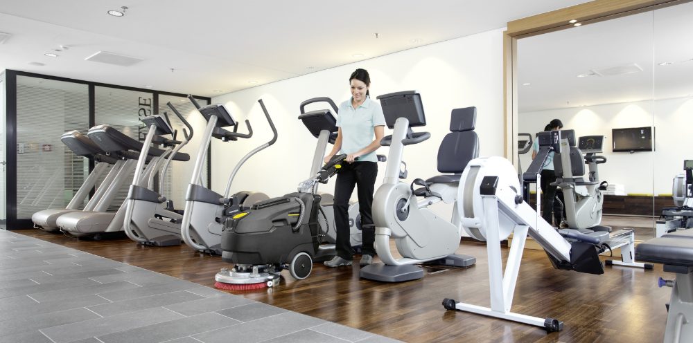 A woman cleans a fitness area with a Kärcher scrubber-dryer