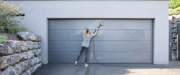 Une femme nettoie sa porte de garage avec une brosse de lavage Kärcher