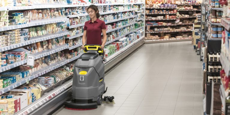 Une femme nettoie une allée du supermarché avec une autolaveuse